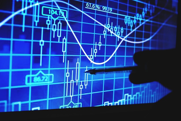 Pluma apuntando con la mano recortada al gráfico azul en el monitor de la computadora