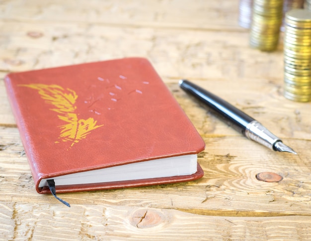 Pluma estilográfica, monedas y cuaderno en una mesa de madera.