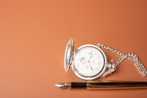 Pluma estilográfica y reloj, hermosos detalles de una pluma estilográfica y un reloj antiguo expuestos sobre una superficie de cuero, enfoque selectivo.