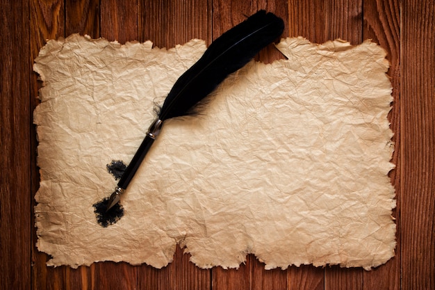 Pluma negra y papel viejo en el fondo de una mesa marrón