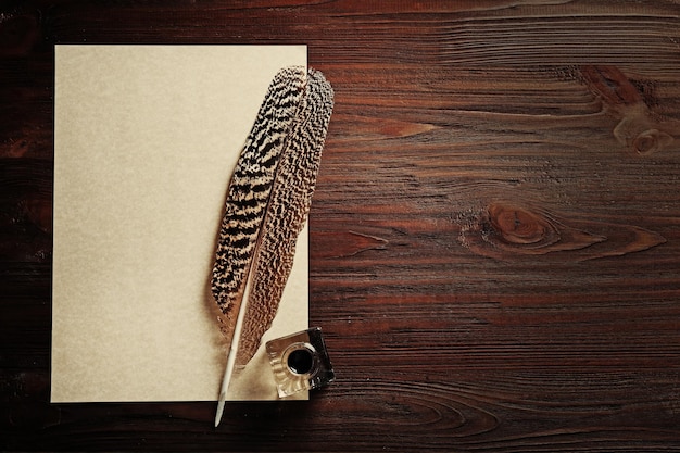 Pluma de pluma con tinte y papel en blanco sobre fondo de madera