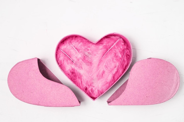 Plumas rosas en caja de regalo en forma de corazón sobre fondo blanco.