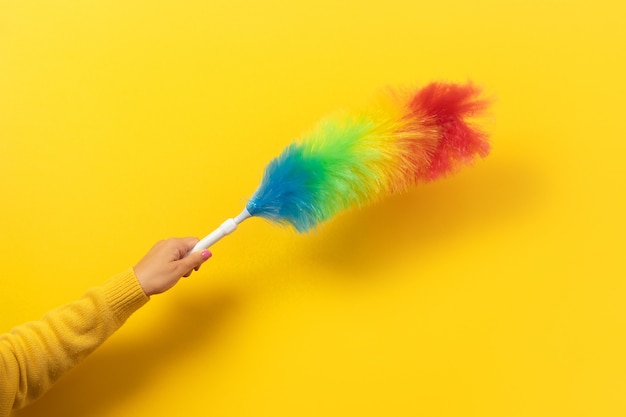 Plumero de plumas de colores en la mano sobre fondo amarillo. Concepto de limpieza.