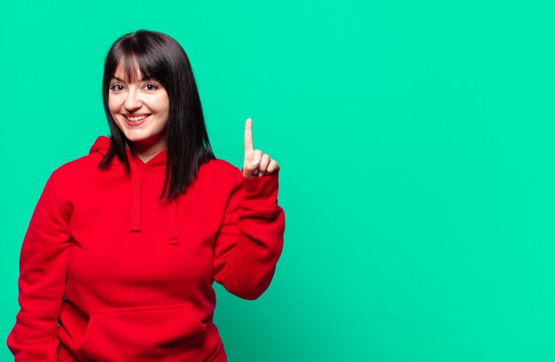 Plus Größe hübsche Frau lächelnd und freundlich aussehend, zeigt Nummer eins oder zuerst mit der Hand nach vorne, Countdown