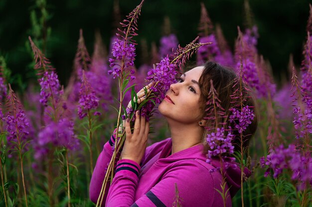 Plus-Size-Frau in fuchsiafarbenem Hoodie, die beiseite steht, während sie inmitten von hellen Blumen auf einer Wiese auf dem Land steht