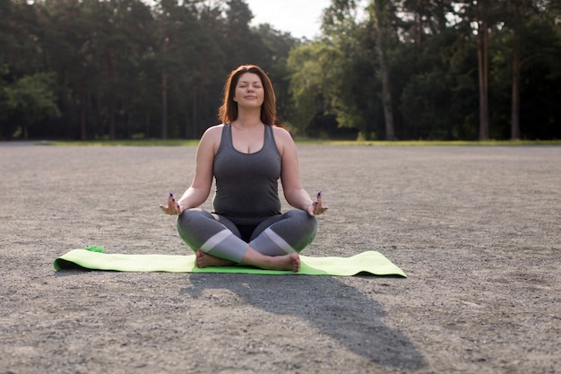Plusgrößenmädchen, das draußen Yoga meditiert