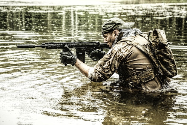 Foto pmc contratista militar privado en la gorra de béisbol durante la incursión del río en la jungla hasta la cintura en el agua y el barro