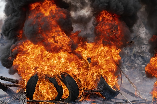 Pneus de automóveis em chamas, forte chama de fogo vermelho e nuvens de fumaça preta no céu. Foco seletivo, desfoque de fogo forte.