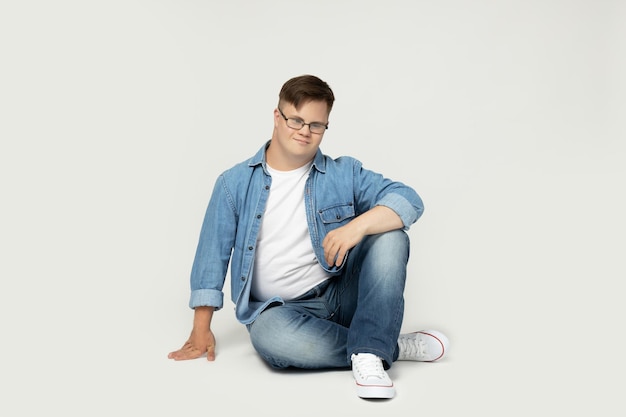 PNGjoven sonriente con síndrome de Down con gafas, vaqueros y camiseta blanca posando para una cámara aislada sobre un fondo blanco