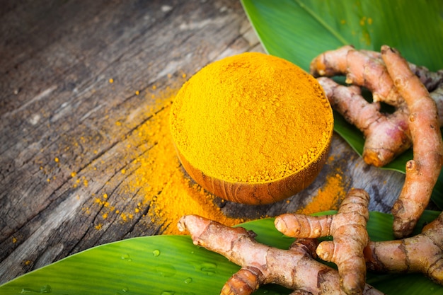 Pó da cúrcuma e cúrcuma fresca em bacias de madeira com a folha verde na tabela de madeira velha. Ervas