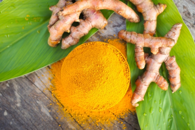 Pó da cúrcuma e cúrcuma fresca nas bacias de madeira na tabela de madeira. Ervas