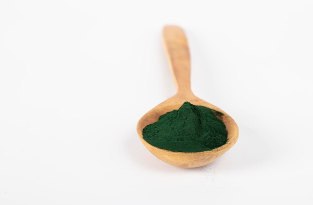 Pó de algas espirulina orgânica na colher de pau no fundo branco.