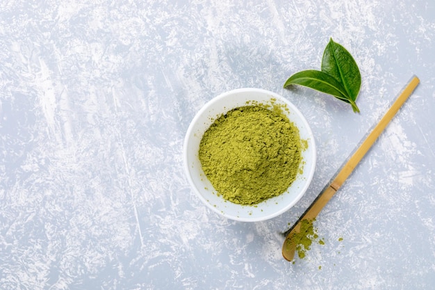 Pó de chá matcha verde asiático em tigela branca folhas de colher de bambu em espaço de cópia de vista superior cinza