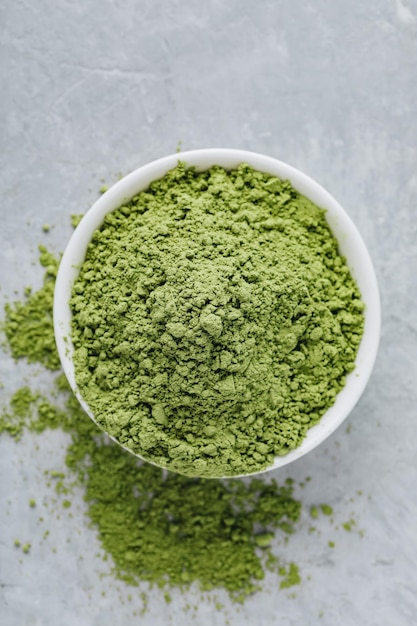 Pó de chá matcha verde em tigela branca sobre fundo de pedra cinza Vista superior