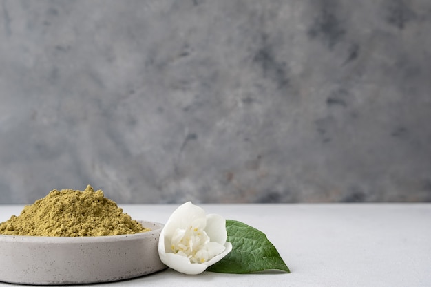 pó de hena para tingir cabelos e sobrancelhas e desenhar mehendi nas mãos em um pedestal de cimento cinza com flores secas ou uma flor branca.