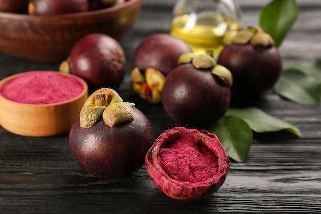 Pó de mangostão roxo e frutas na mesa de madeira preta