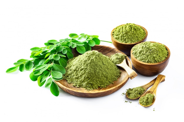 Pó de moringa (moringa oleifera) em uma tigela de madeira com as folhas frescas originais de moringa, isoladas no branco.