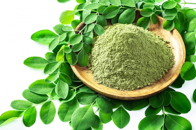 Pó de moringa (moringa oleifera) em uma tigela de madeira com as folhas frescas originais de moringa, isoladas no branco.