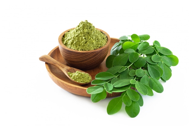 Pó de moringa na bacia de madeira com as folhas frescas originais de moringa isoladas no fundo branco.