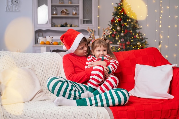 Época de Natal. filhos bonitos irmão e irmã de pijama de natal abraçados juntos no sofá