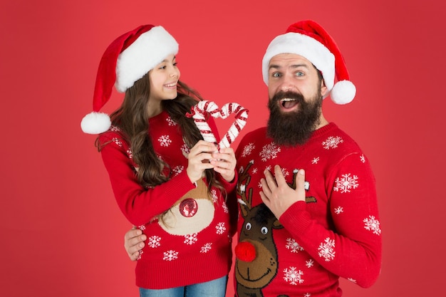 Época de Natal para bondade e bondade. Canção de Natal. Pai e filha com decorações de Natal de bastões de doces. Feriado familiar. Aparência da família do Papai Noel. Pai barbudo e uma menina alegre.