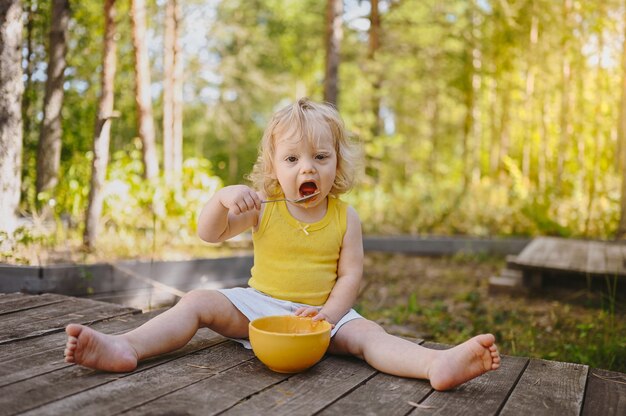 Poco gracioso lindo niño niña rubia con ropa sucia y cara comiendo fruta de comida para bebés o