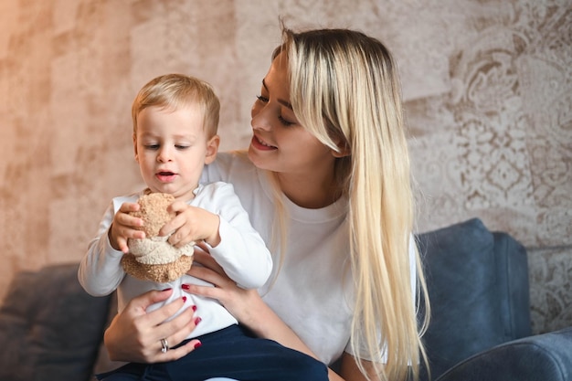 Poco lindo bebé niño rubio sentado en los brazos de las madres hermosa joven mamá e hijo jugando