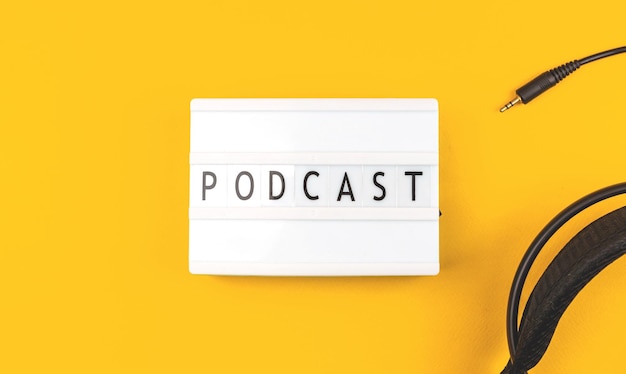 Foto podcast-wort auf gelbem tischhintergrund des leuchtkastens mit draufsichtfoto der kopfhörer