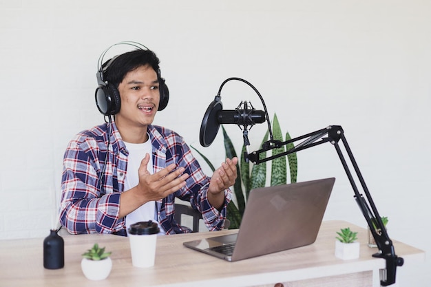 podcaster explicando información usando una computadora portátil y un micrófono transmitiendo en línea en el estudio de casa