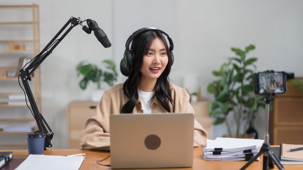 La podcaster femenina usa un teléfono inteligente y habla con la audiencia en el micrófono para grabar un podcast de video