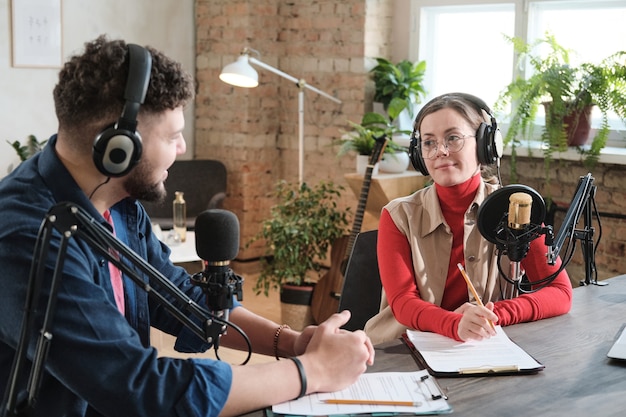 Foto podcasters conversando com microfones gravando podcast em estúdio