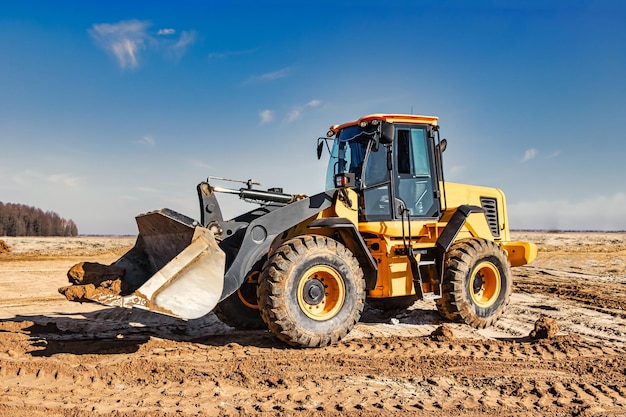 Poderoso trator ou carregador move a terra no canteiro de obras contra o céu uma máquina de terraplenagem está nivelando o local equipamento pesado de construção para terraplanagem