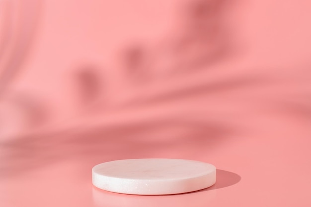 Pódio de mármore branco no fundo rosa com sombra de plantas tropicais. Pódio para produto, apresentação cosmética. Mock up criativo. Pedestal ou plataforma para produtos de beleza.