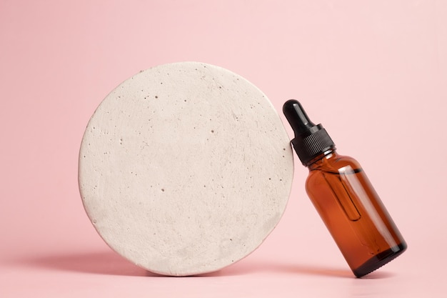 Pódio de pedra de frasco conta-gotas de vidro em fundo rosa Produtos para a pele cosméticos naturais Conceito de beleza para cuidados com o rosto e o corpo