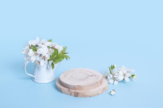 Podio de madera o pedestal con flores de cerezo en una regadera sobre fondo azul Mock up para productos cosméticos