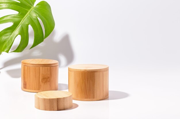 Podios de madera para la exhibición de productos y hojas de monstera sobre fondo blanco