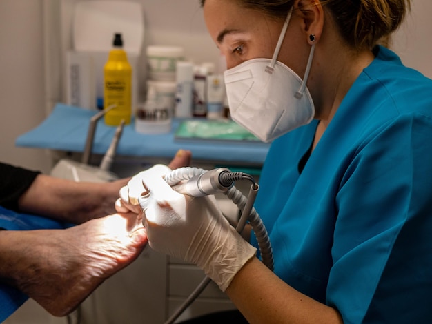 Podólogo feminino em uma máscara médica e luvas tratando os pés de um cliente