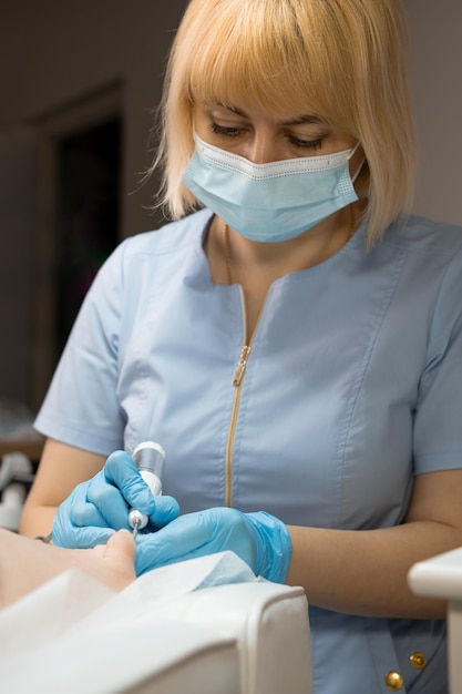 Foto podólogo con máscara facial durante el proceso de extirpación de una uña de pie encarnizada