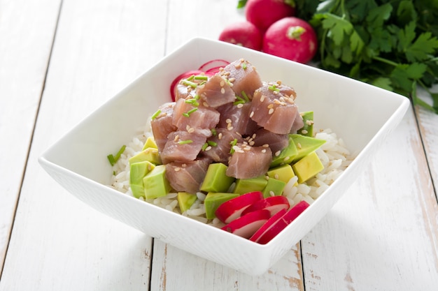 Poke Bowl de atún hawaiano con aguacate, rábanos y semillas de sésamo en mesa de madera blanca