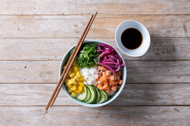 Poke bowl com arroz salmão pepino mangoonion wakame salada sementes de papoula e sementes de girassol em fundo de madeira