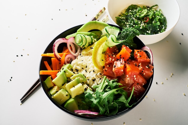 Poke Bowl mit Lachs, Avocado, Gurke, Rucola, Broccoli, Reiskarotte mit Chuka-Salatessstäbchen