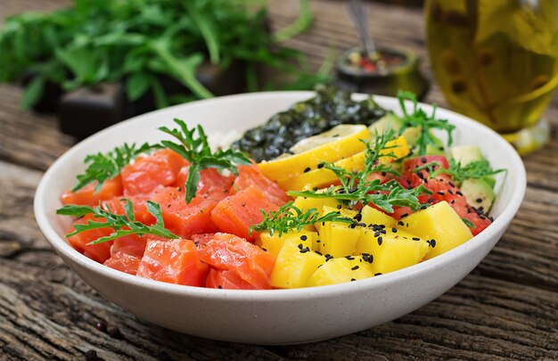 Poke bowl de salmón hawaiano con arroz, aguacate, mango, tomate, semillas de sésamo y algas. Tazón de Buda. Comida dietetica.