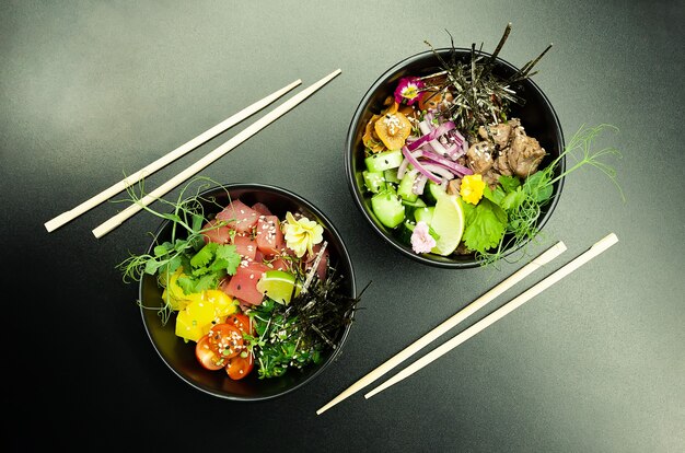 Poke saladas com atum e carne em tigelas sobre a mesa duas tigelas de poke salada com pauzinhos em um gr ...