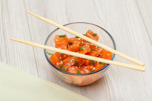 Poke de salmón hawaiano con cebollas verdes y semillas de sésamo en un recipiente de vidrio con palillos Vista superior