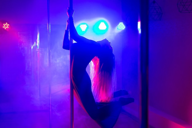 Pole dance. Joven esbelta sexy bailando en un poste en el interior de una discoteca