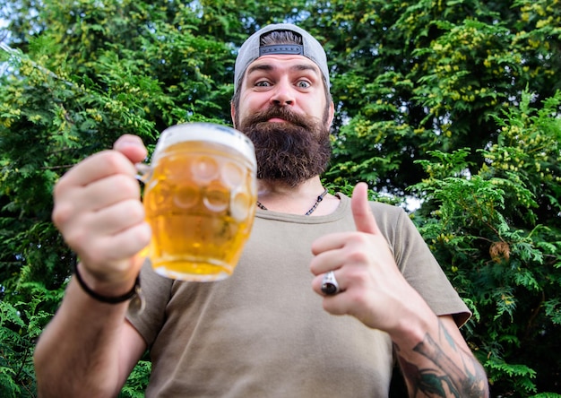 Polegares até o melhor bebedor de cerveja Homem segurando caneca de cerveja Homem barbudo gosta de beber cerveja na natureza Hipster brutal com barba longa tomando cerveja artesanal