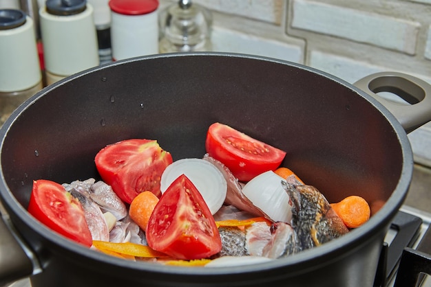 Poleiro de peixe é cozido no caldeirão com tomates, cenouras e cebolas no fogão a gás