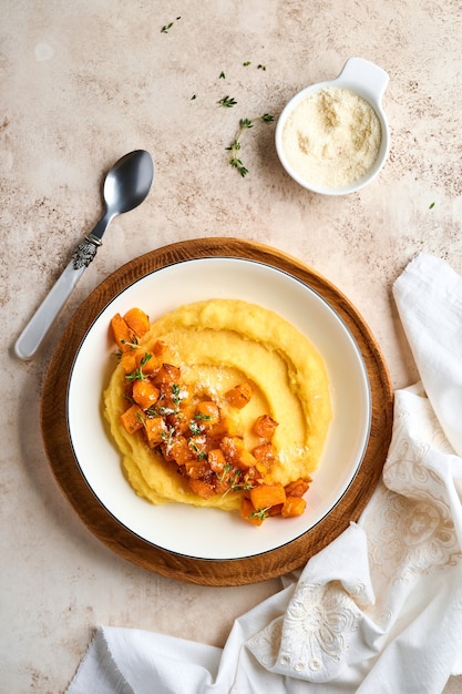 Polenta con mantequilla, calabaza, ajo, ajedrea y queso parmesano en un tazón blanco sobre fondo de hormigón claro. Comida tradicional italiana básica, comida vegana. Vista superior. Copie el espacio.