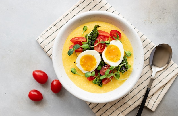 Polenta-Schüssel mit frischem Gemüse Microgreens und Eiern auf grauem Tisch gesundes ausgewogenes Frühstück