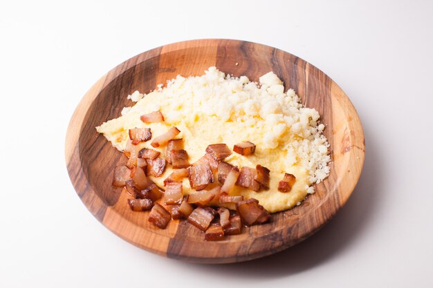 Polenta con tocino y queso salado en la mesa de madera - plato tradicional de los Cárpatos